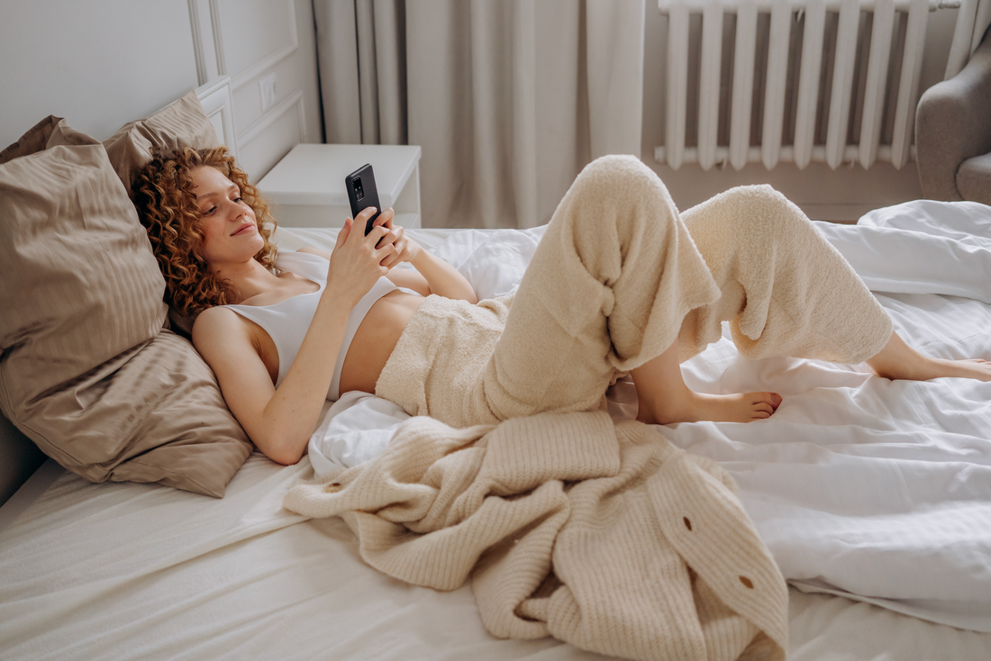 lady with curly hair researching how to remove stains from bed sheets while laying in bed